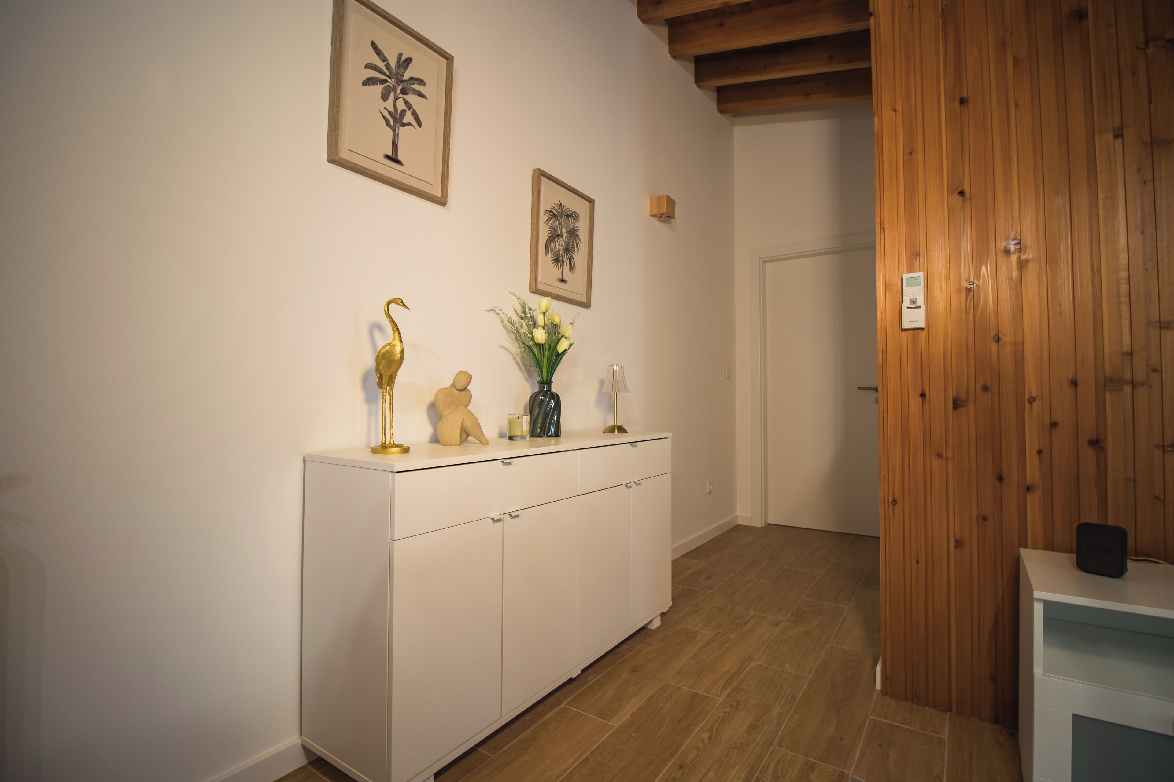 A hallway with a white cabinet, a wooden door, and two framed pictures on the wall.