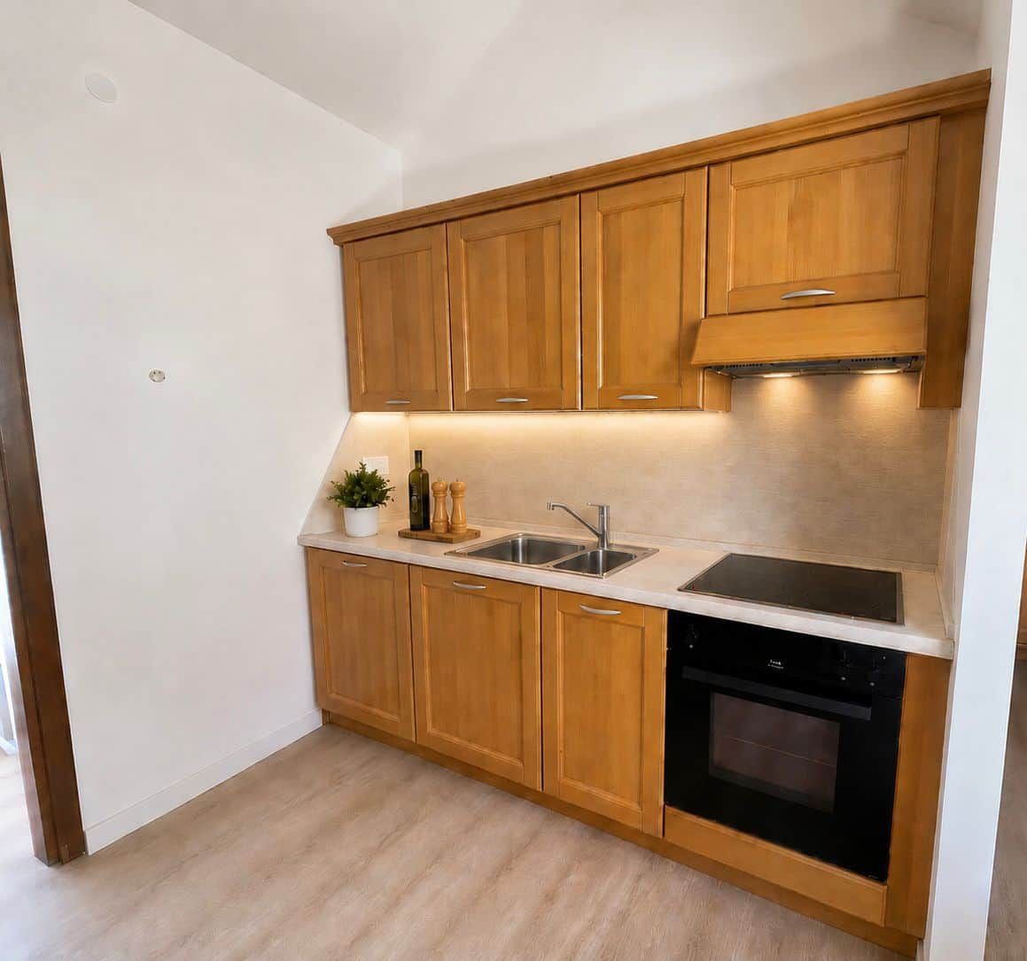Une cuisine compacte avec des meubles en bois, un évier à deux bacs et un four encastré.