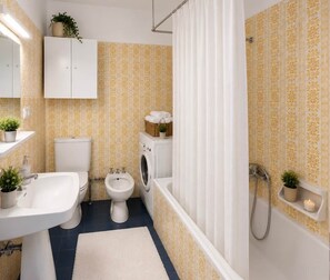 A bathroom with a toilet, bidet, washing machine, and bathtub. - Oria Dolomites Stay (Alba)
