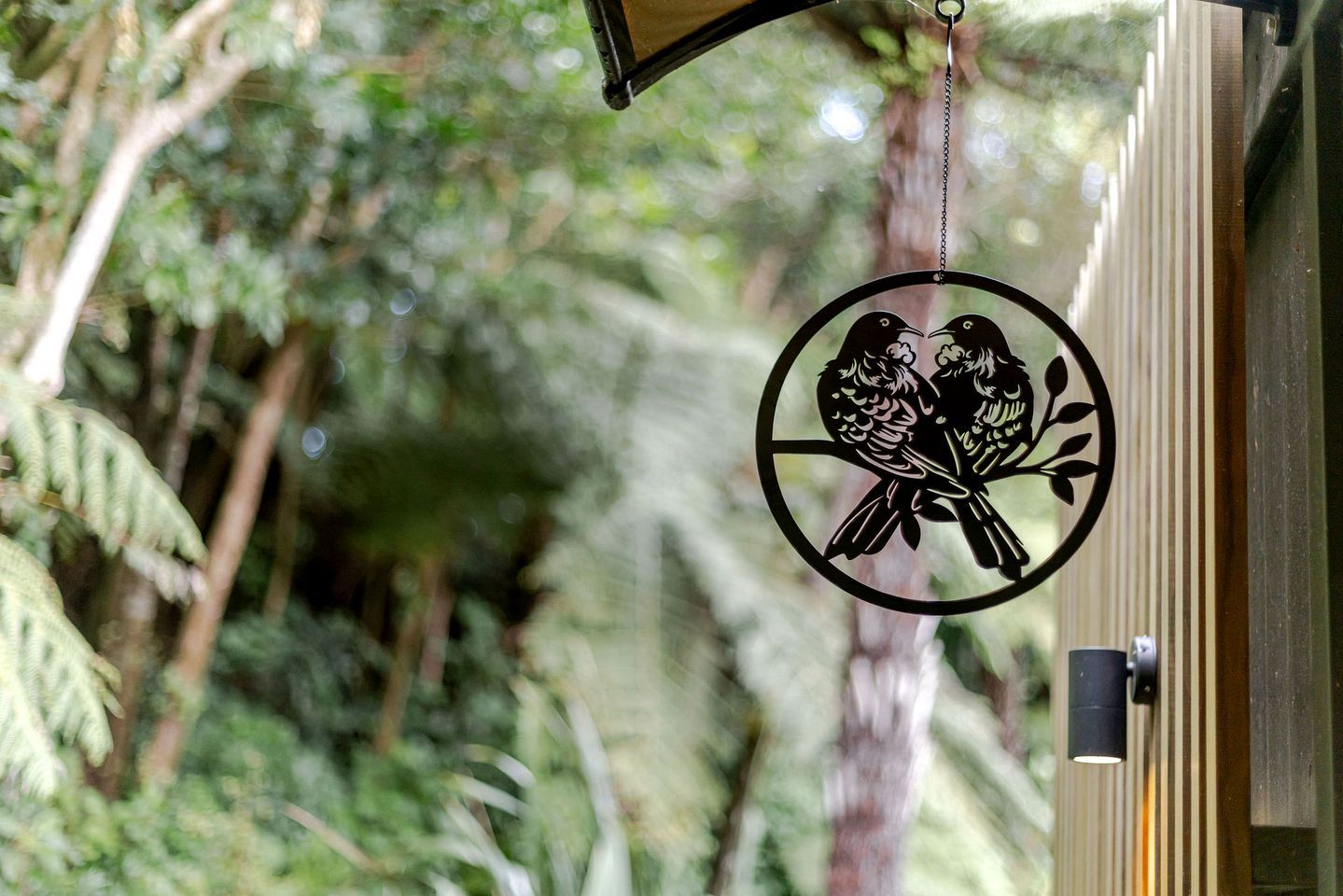 A circular metal ornament with a bird design, hanging near a window with a blurred natural background.