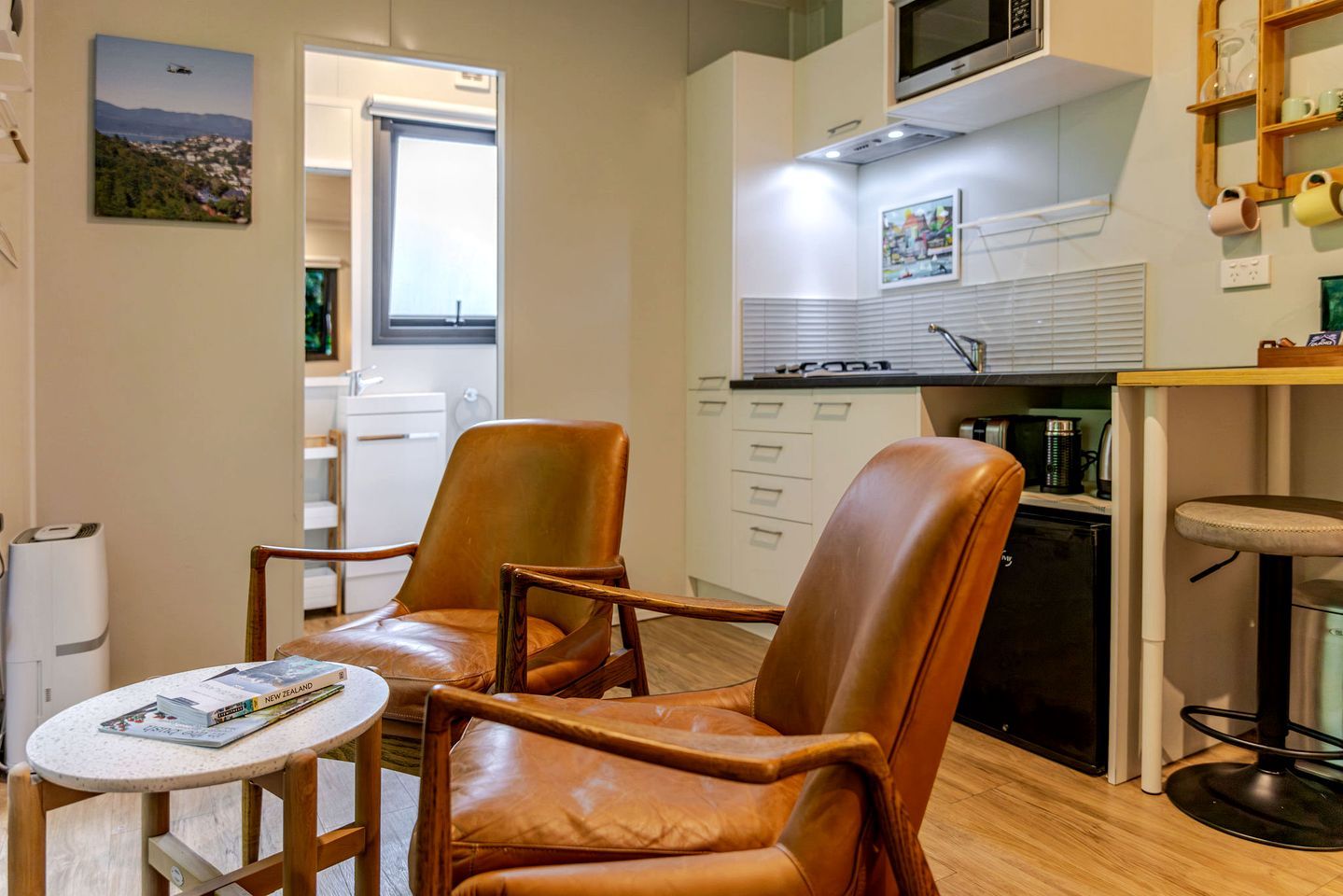 A compact living space with a kitchenette, two leather chairs, a small round table, and a view of the outside.