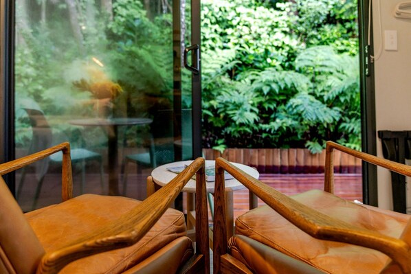 A seating area with wooden chairs and a round table, overlooking a lush garden through a glass door.