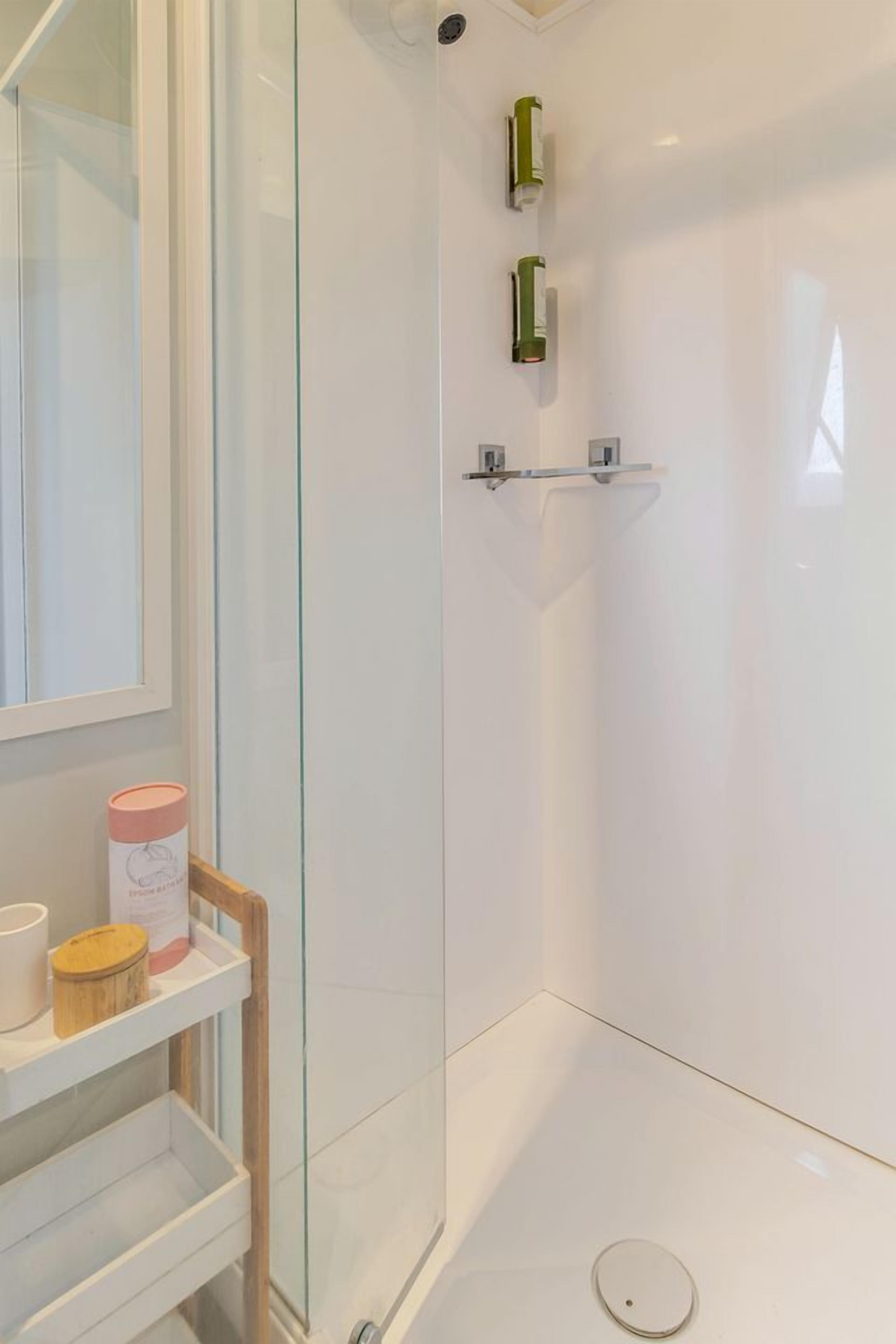 A modern bathroom with a glass shower enclosure, a white sink, and a shelf with toiletries.