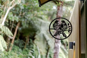 Adorno metálico circular con diseño de pájaro, colgando cerca de una ventana y un fondo natural borroso.