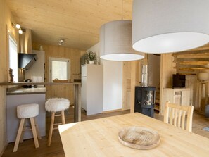 A modern kitchen with wooden accents, a dining table with stools, and a large pendant light. - One-bedroom Cabin (Sankt Georgen am Kreischberg)