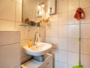 Een moderne badkamer met een witte wastafel, een glazen plank en een dweil die tegen de muur staat.