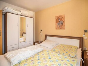 Een slaapkamer met een bed, een kledingkast, een nachtkastje en een wandlamp.