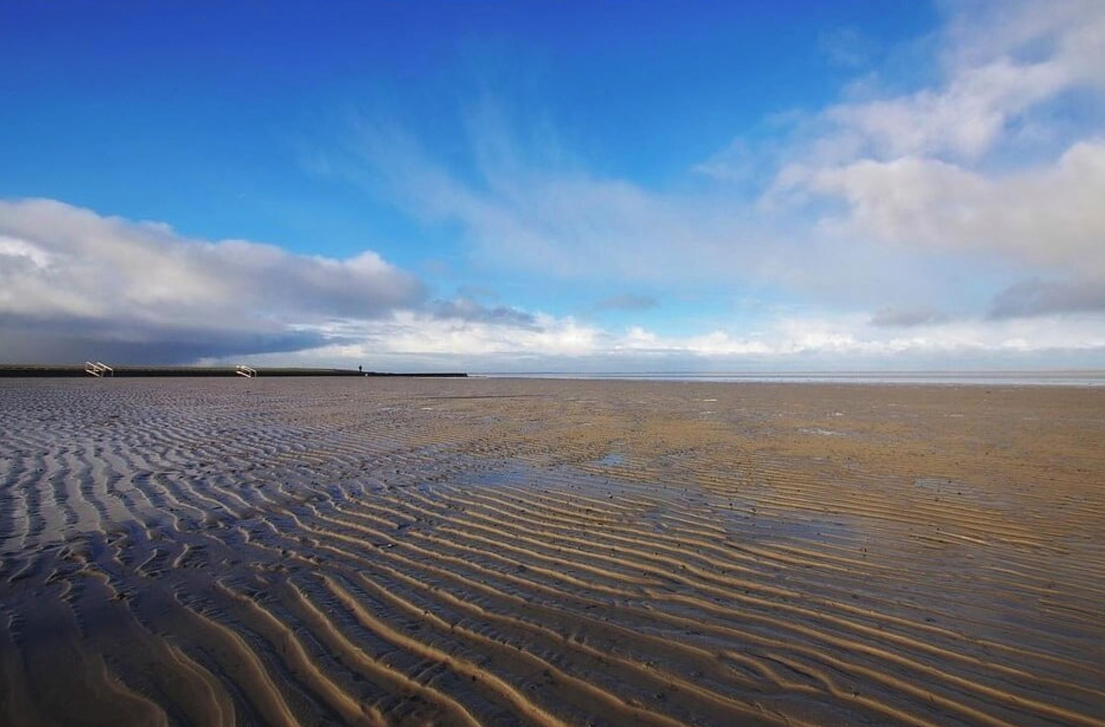 Une plage avec des ondulations dans le sable et un ciel dégagé.