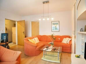 A living room with a sectional sofa, a glass coffee table, and a pendant light fixture. - Niedl App Helene 1 (Dornum)