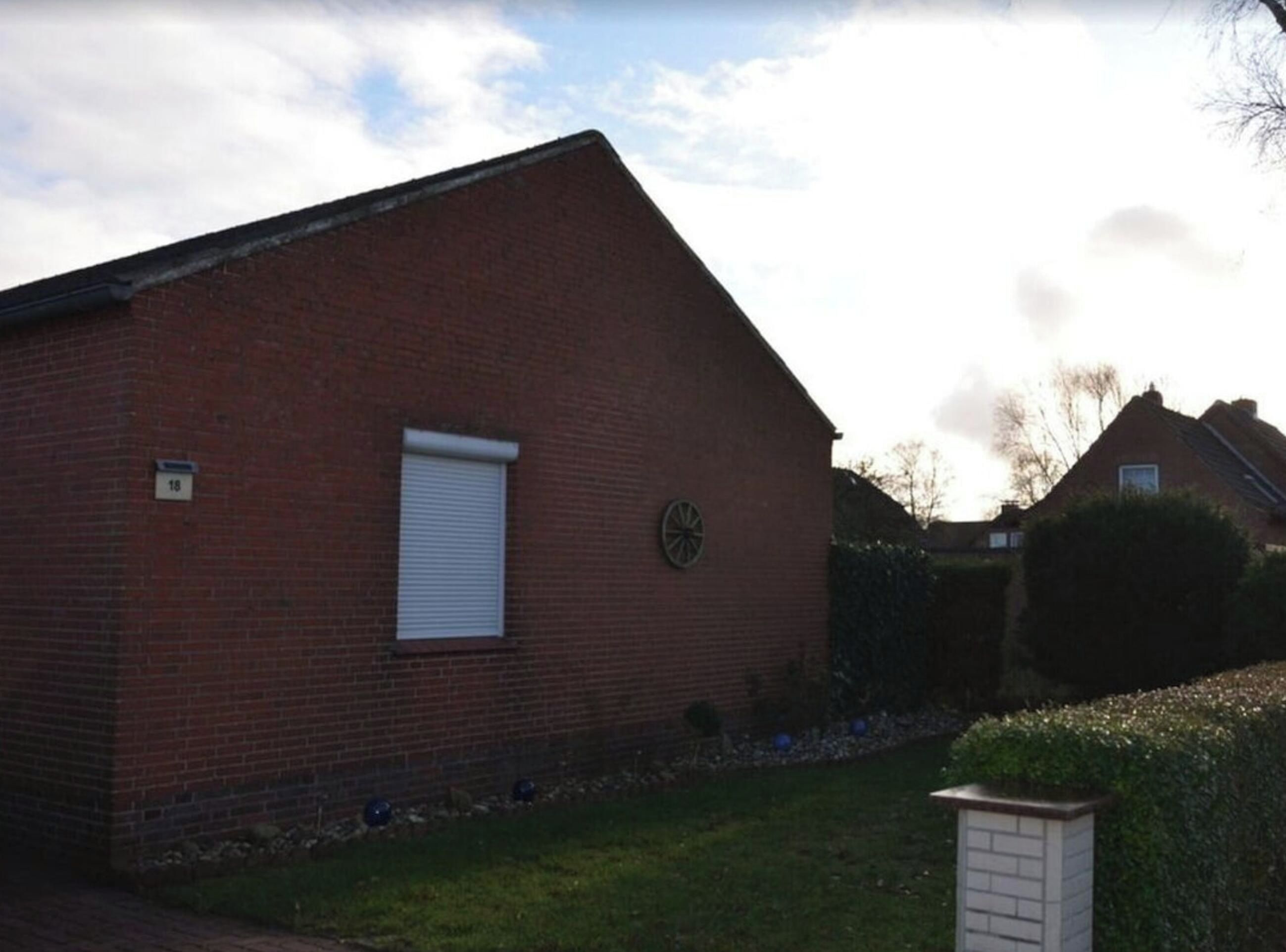 A brick building with a closed shutter, a small circular window, and a number '18' sign on the wall.
