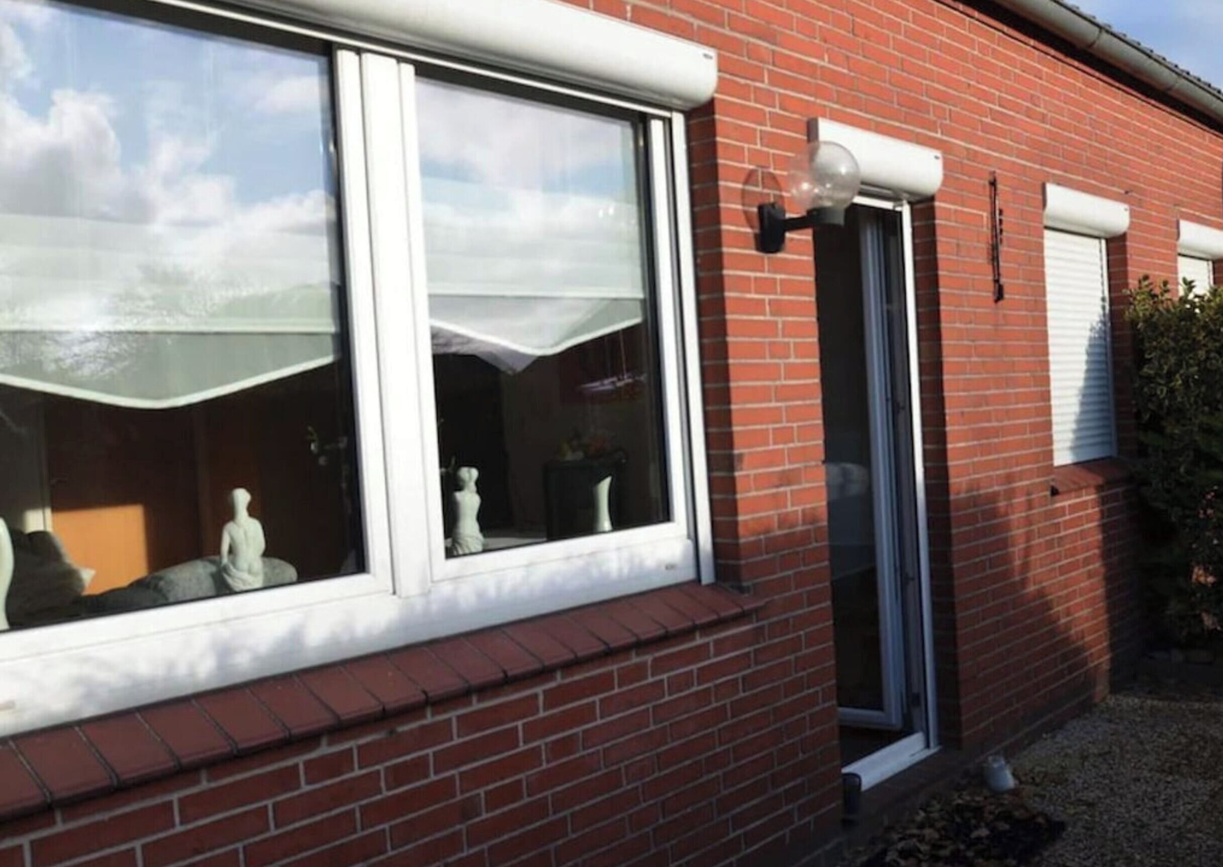 Une maison en briques avec une grande fenêtre et une porte plus petite, toutes deux dotées de cadres blancs.