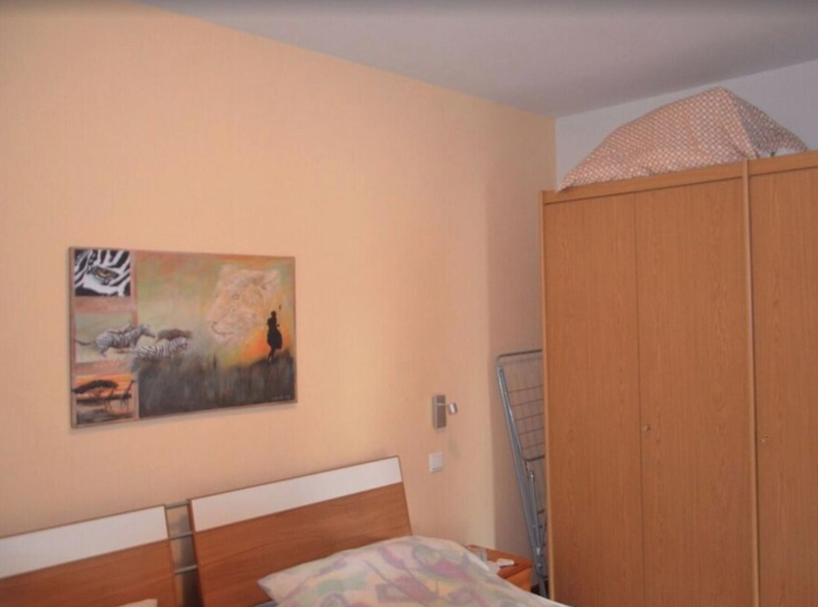 A bedroom with a bed, a wardrobe, and a painting on the wall.
