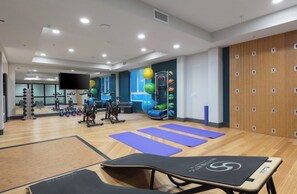 Ein Fitnessraum mit Trainingsgeräten, Matten und Schließfächern.