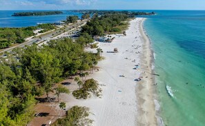 Ein Strand mit einer parallel verlaufenden Straße, umgeben von Bäumen und freiem Blick auf den Ozean.