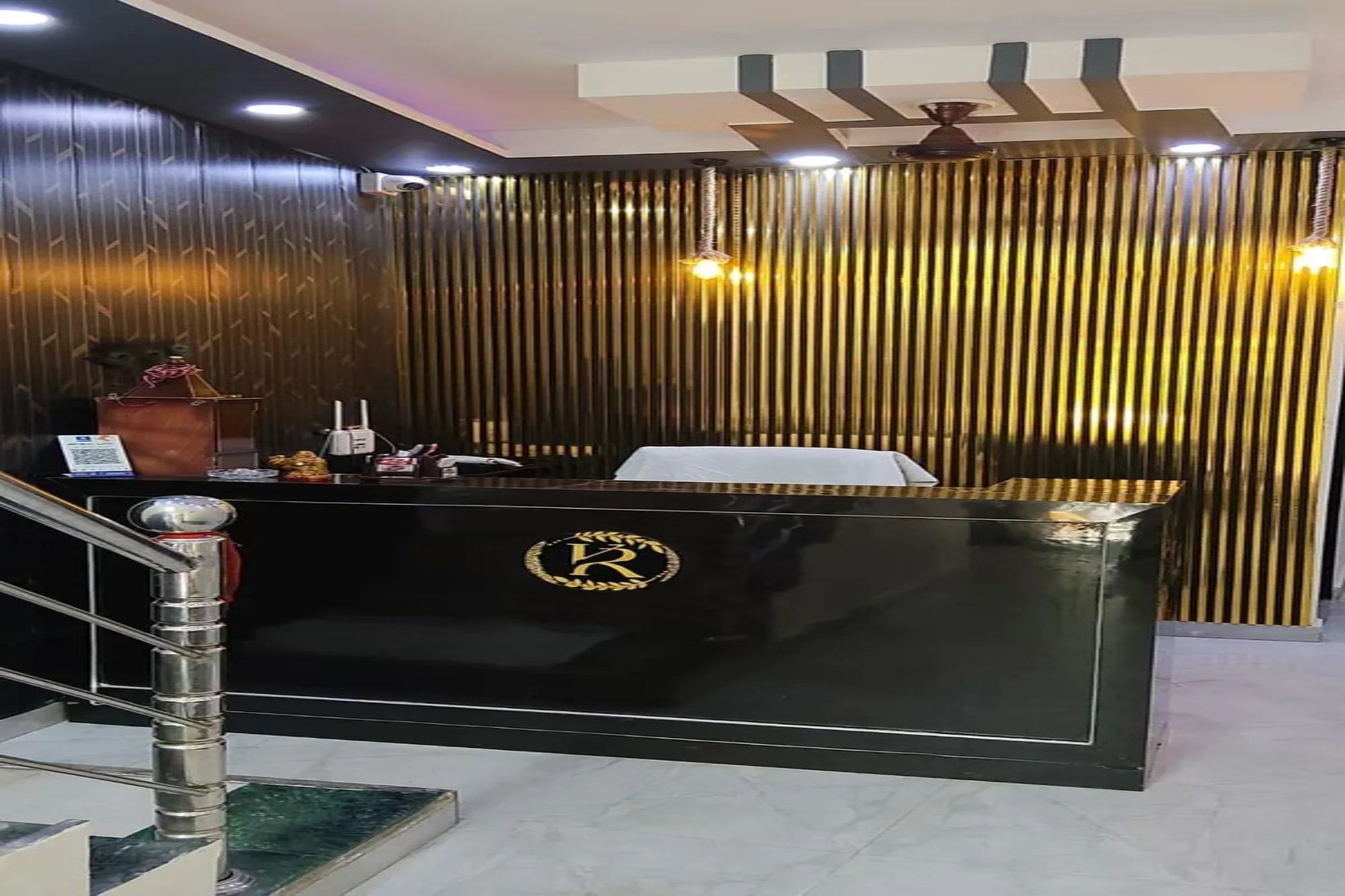 Un mostrador de recepción con un logotipo, una escalera y una pared con persianas verticales.