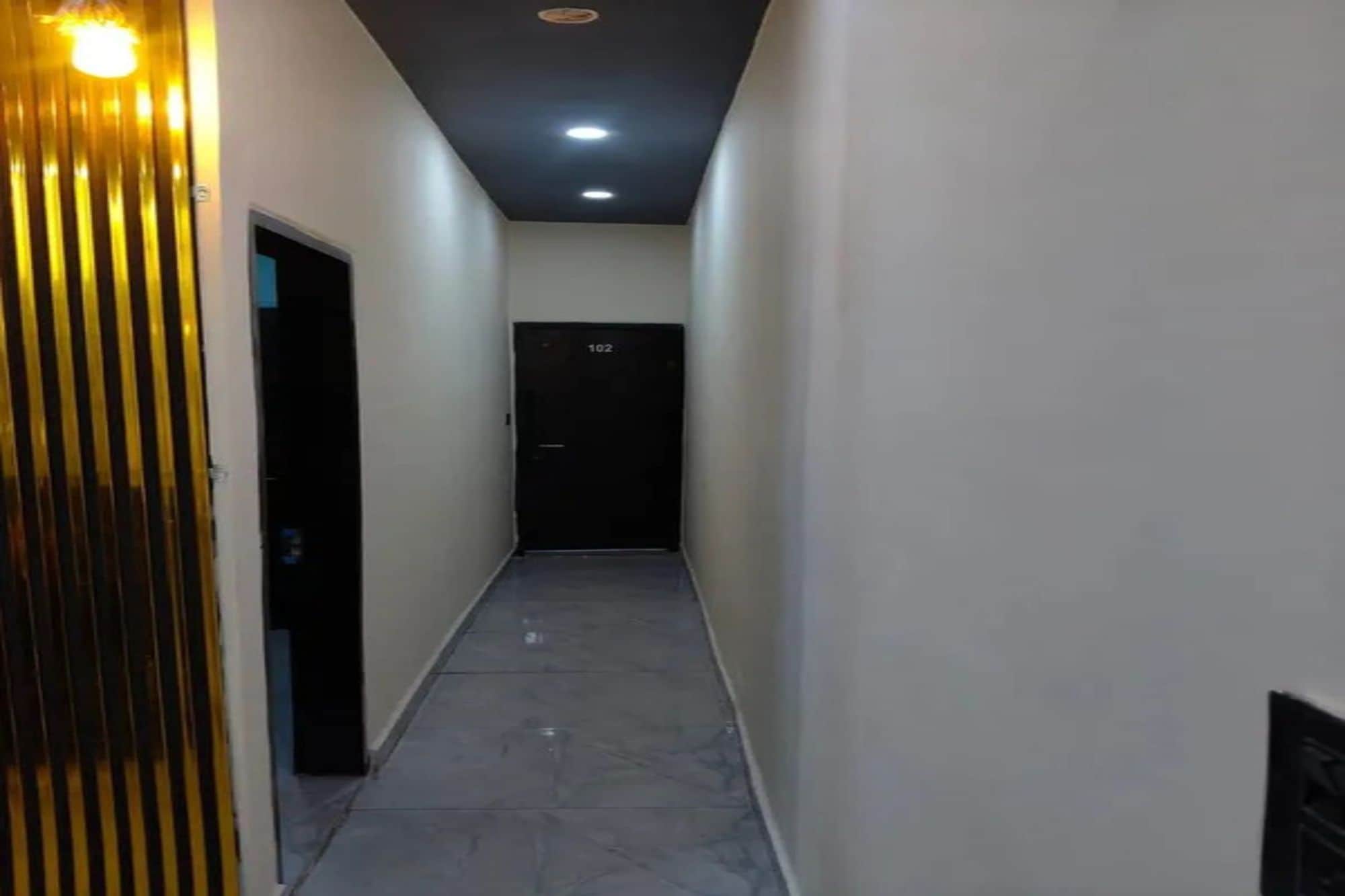 Un pasillo estrecho con una puerta marcada '02' al final, que conduce a una habitación oscura.