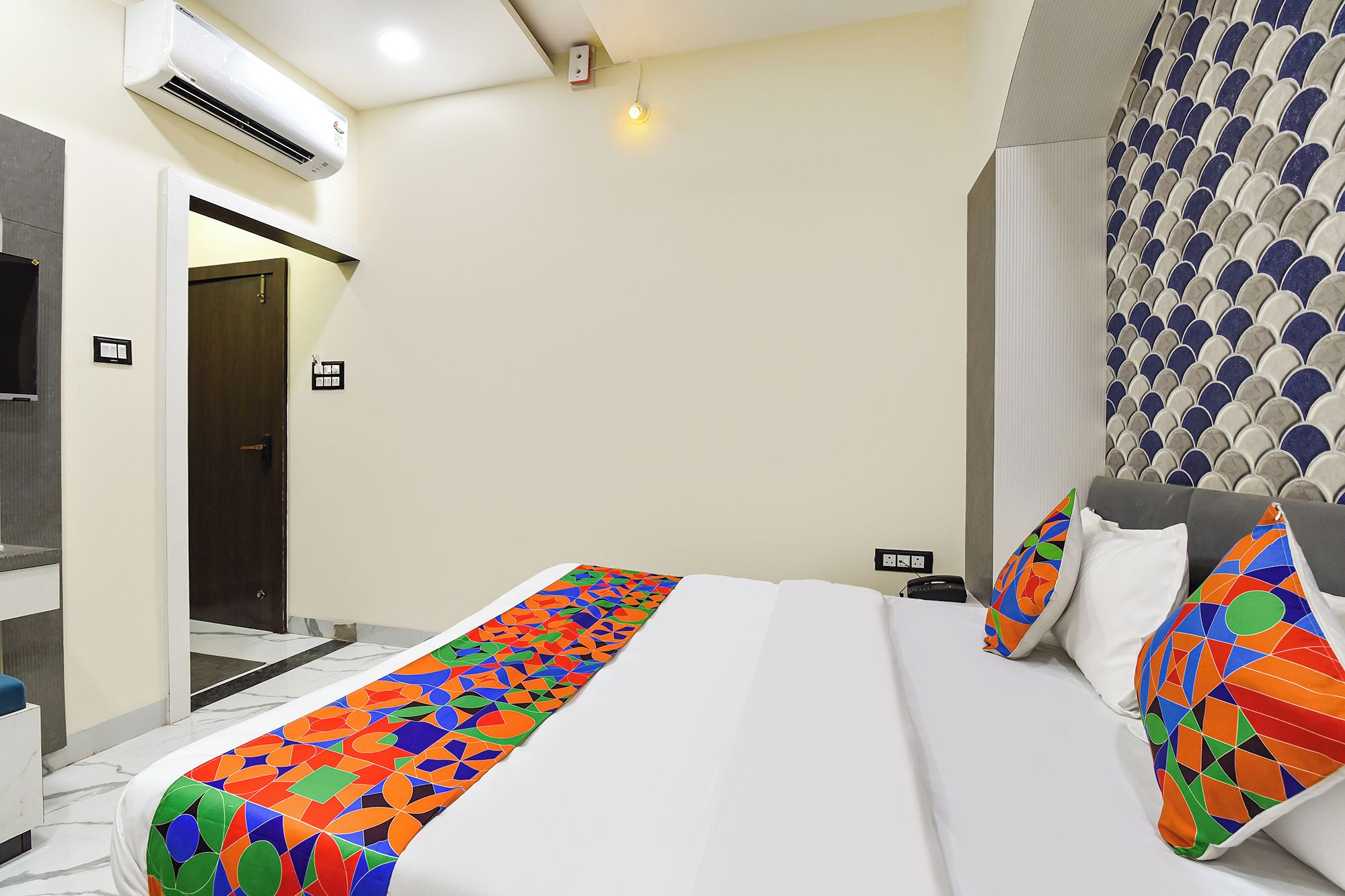 Habitación de hotel con cama, mesita de noche, equipo de aire acondicionado, una puerta y pared con diseño estampado.