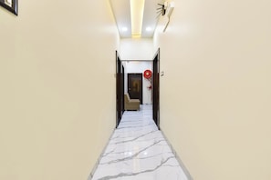 A hallway with a marble floor leading to a room with a bed and a red fire extinguisher. - Fabhotel B1 (Indore)