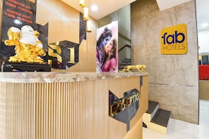 A hotel reception desk with a sign for Fab Hotels, a check-in/out schedule, and a reception area with a marble wall and a staircase. - Fabhotel B1 (Indore)