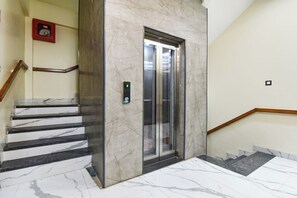 Una escalera de mármol que conduce a un ascensor con panel de control digital.