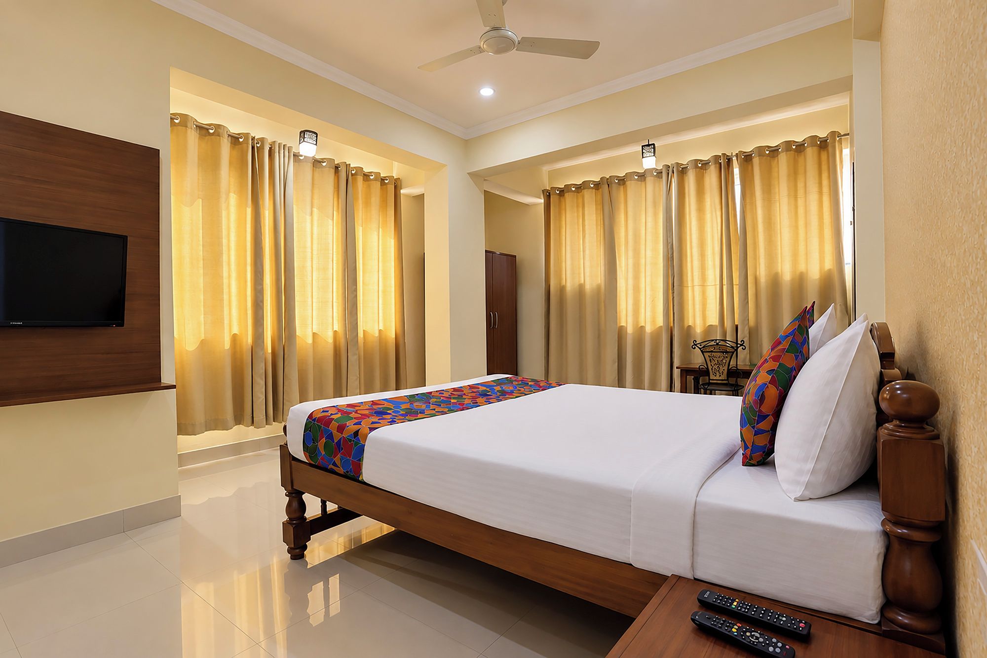 Quarto de hotel com cama, cortinas, televisão e ventoinha no teto.