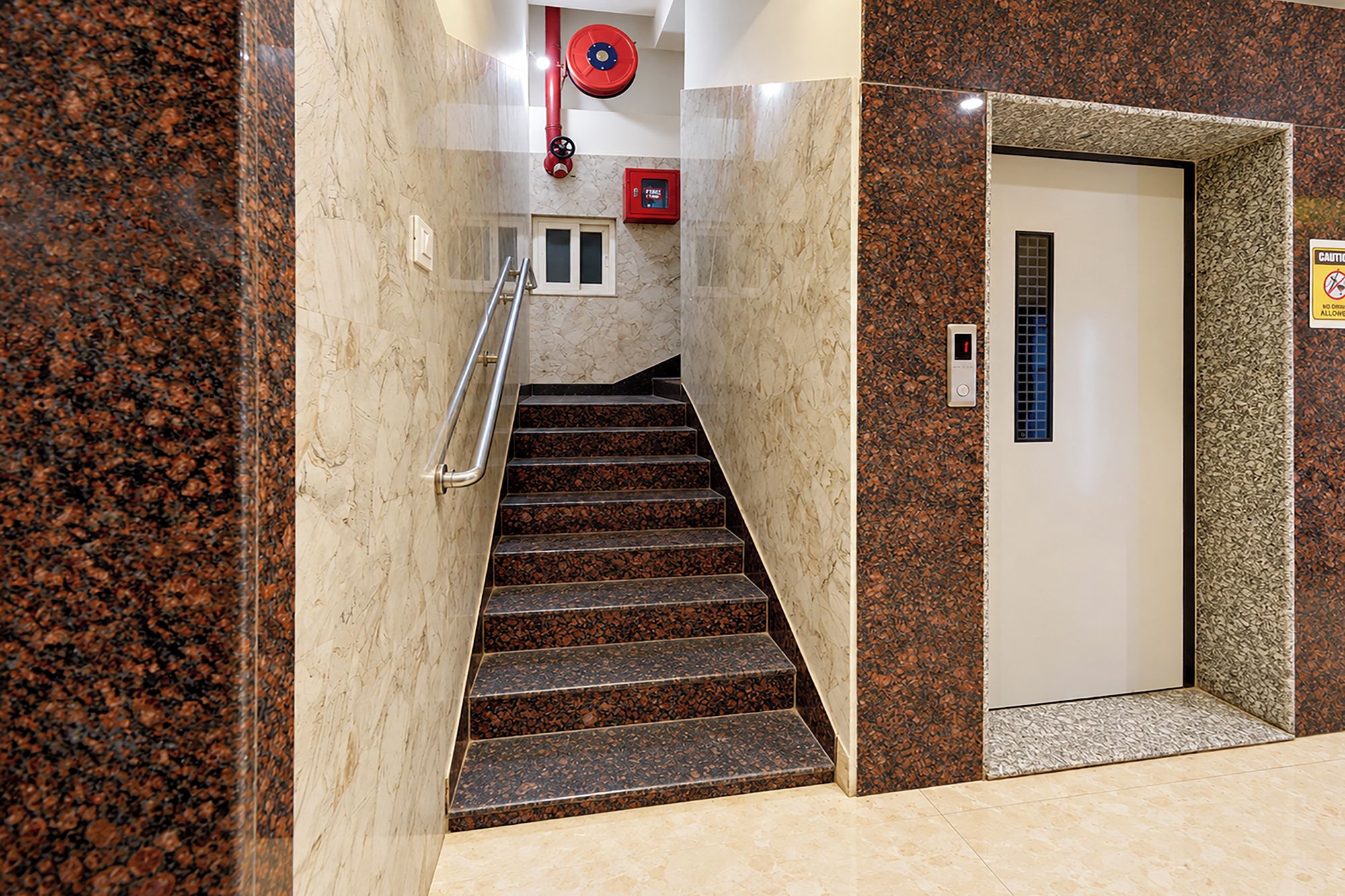 A staircase with a handrail, a fire alarm, and an elevator door with a control panel.