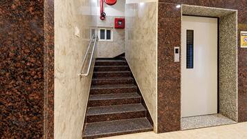 A staircase with a handrail, a fire alarm, and an elevator door with a control panel.