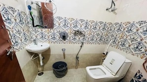 Casa de banho pequena com lavatório branco, sanita e chuveiro. Tem um painel de azulejos estampados e um espelho pequeno sobre o lavatório.