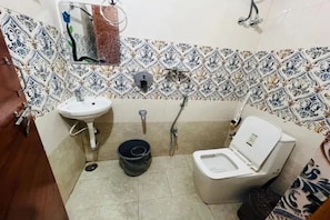 A small bathroom with a white sink, a toilet, and a shower. There is a patterned tile backsplash and a small mirror above the sink. - Fabhotel Vajra Residency (Mancherial)