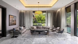 Uma sala de estar moderna com piso de mármore, um conjunto de sofás, uma mesa de centro e uma grande janela com cortinas.