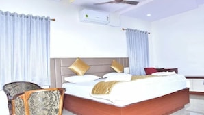 Quarto de hotel com uma cama grande, uma cadeira de madeira, uma escrivaninha e um ventilador de teto.