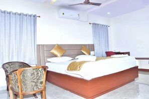 A hotel room with a large bed, a wooden chair, a desk, and a ceiling fan. - Fabhotel Vajra Residency (Mancherial)