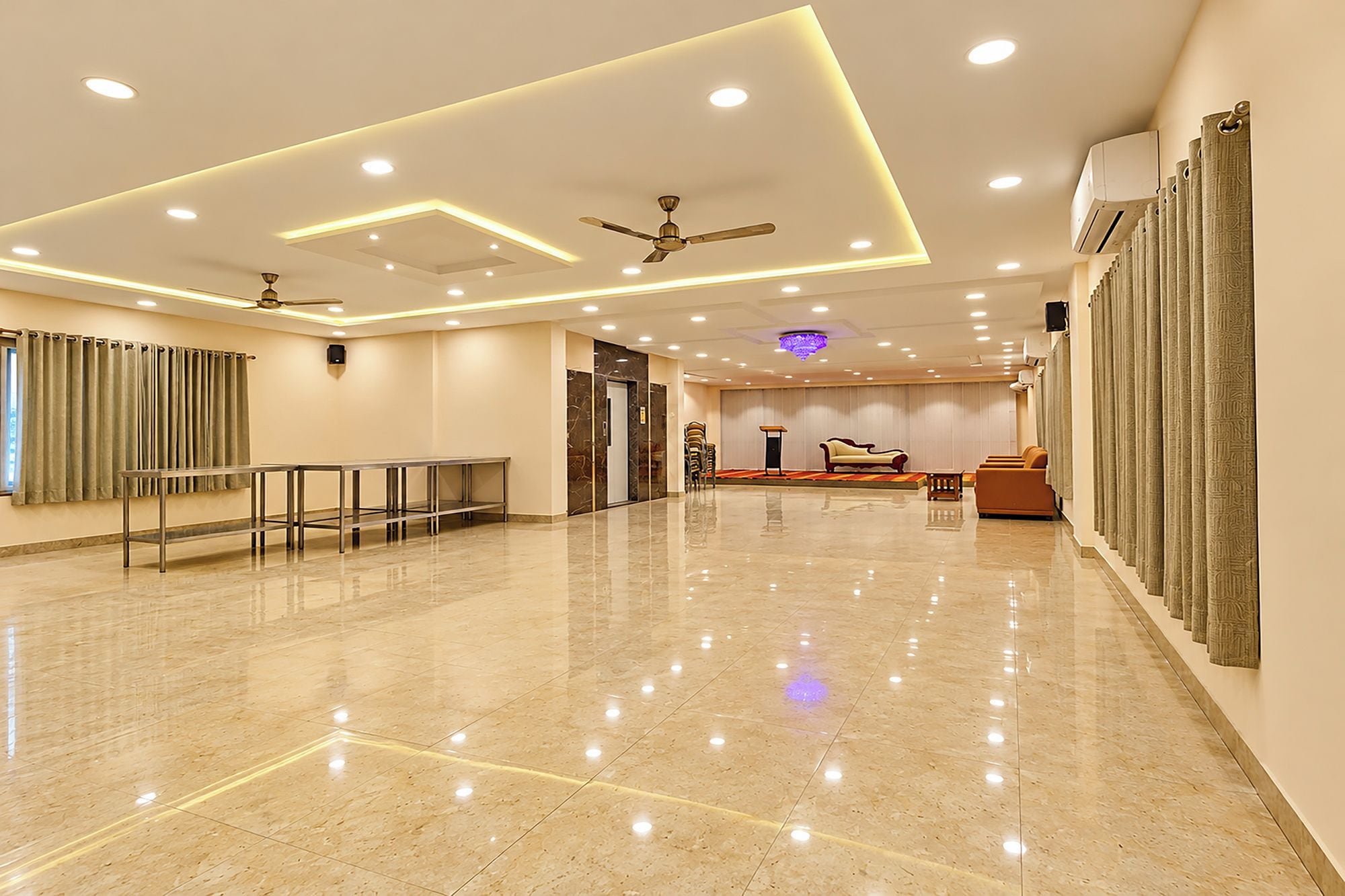 A spacious hotel lobby with a polished marble floor, ceiling fans, recessed lighting, and a seating area with sofas and a coffee table.