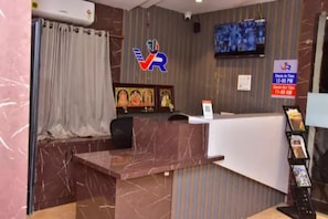 A reception desk with a marble top, a television mounted on the wall, and a check-in/out sign. - Fabhotel Vajra Residency (Mancherial)