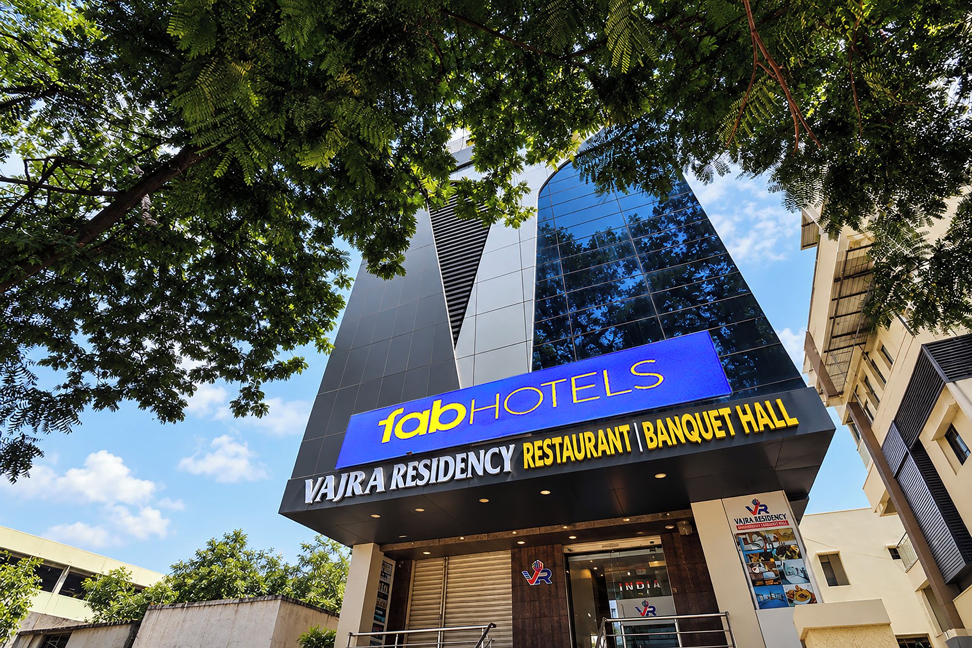 Un edificio con un letrero que dice 'fab hotels' y 'Vajra Residency Restaurant | Salón de banquetes'.