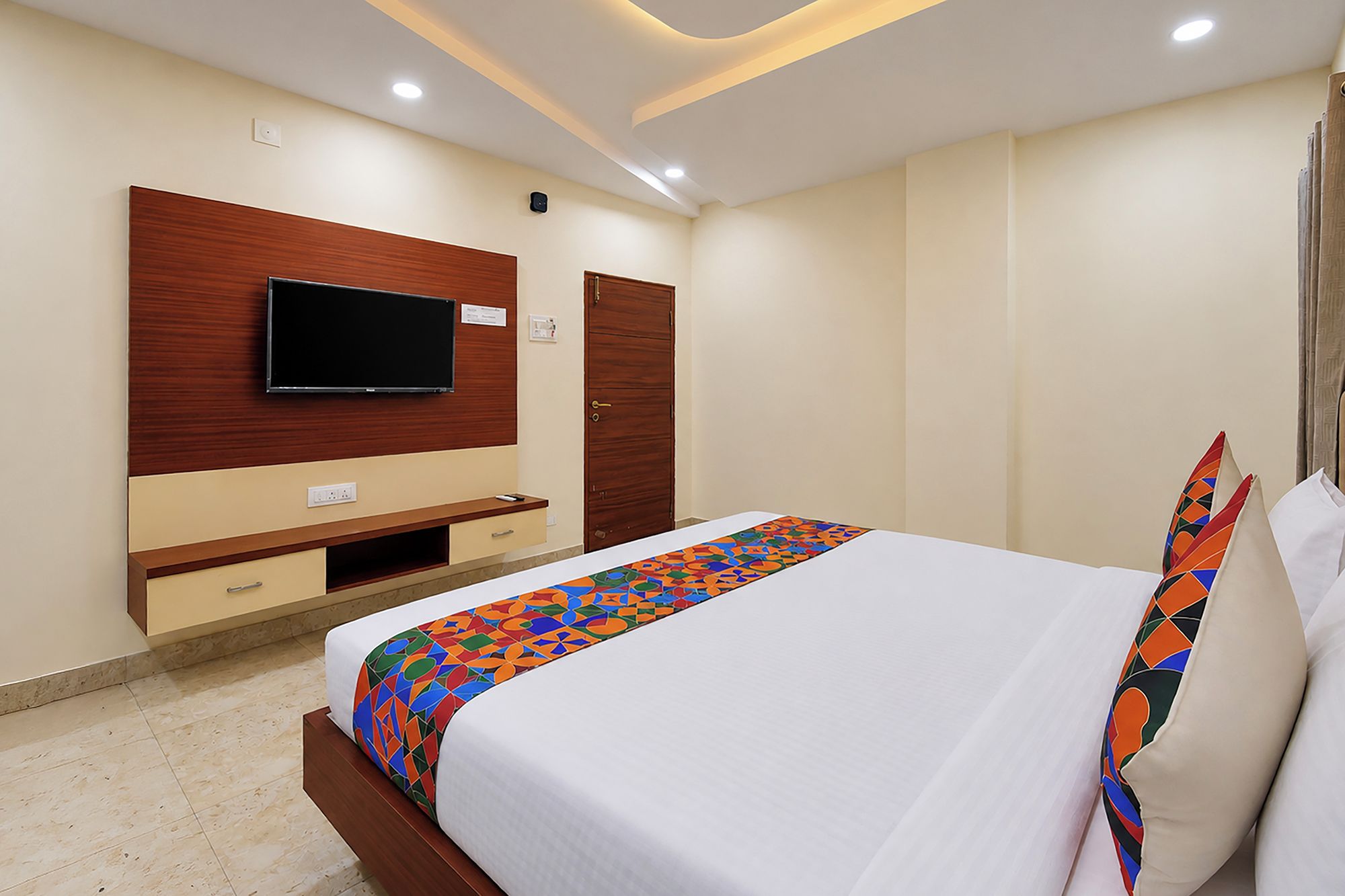 Quarto de hotel com cama, televisão na parede, guarda-roupa e mesa de cabeceira.