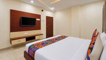 Quarto de hotel com cama, televisão na parede, guarda-roupa e mesa de cabeceira.