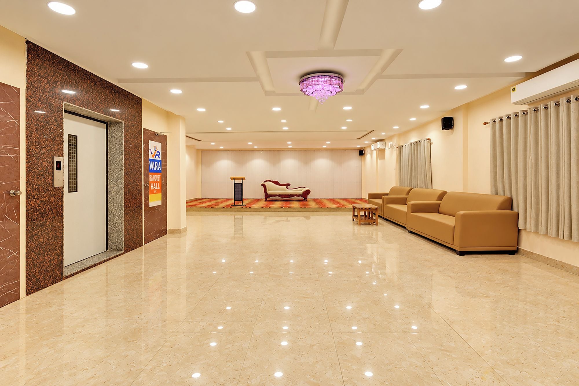 A hotel lobby with a marble floor, a reception desk, a sofa, and a chandelier.