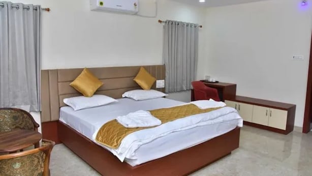 Quarto de hotel com uma cama grande, uma mesinha de cabeceira, uma cadeira e um guarda-roupa.