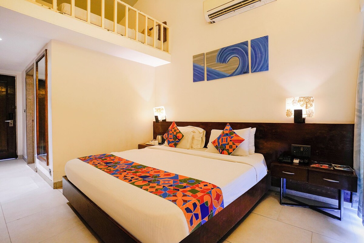 Una habitación de hotel con una cama grande, una mesita de noche, un escritorio, una silla, un balcón y un cuadro en la pared.