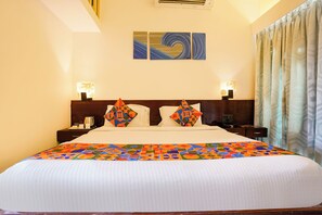 Habitación de hotel con una cama grande, dos almohadas, una mesita de noche con lámpara y un cuadro en la pared.