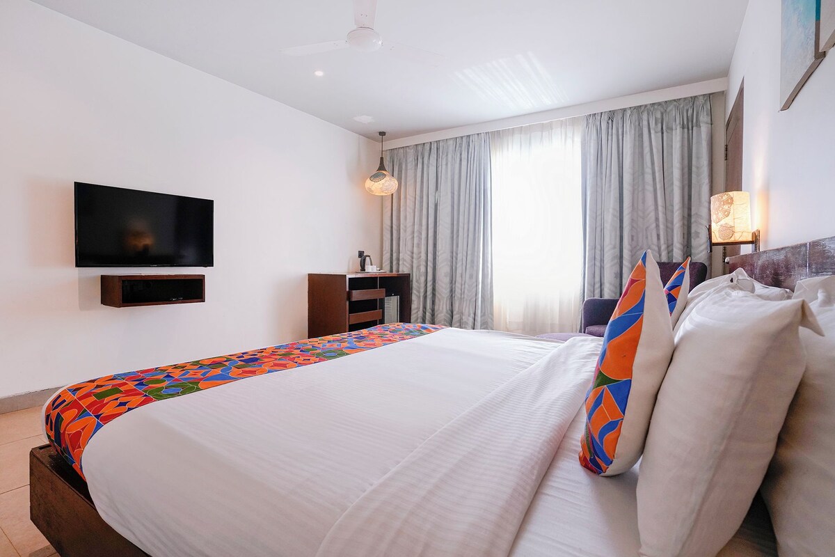 Habitación de hotel con cama, televisión, escritorio y ventana con cortinas.