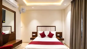 A hotel room with a bed, bedside tables, a desk, a chair, a mirror, and a window with curtains. - Fabhotel Royal Suites (Bangalore)