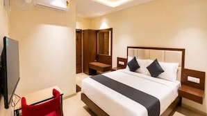 A hotel room with a bed, bedside tables, a red chair, a TV, and a wardrobe. - Fabhotel Royal Suites (Bangalore)