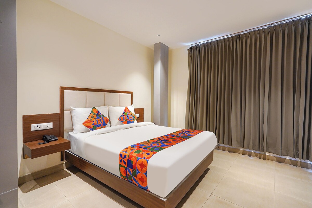Una habitación de hotel con una cama, una mesita de noche, un teléfono y una ventana con cortinas.