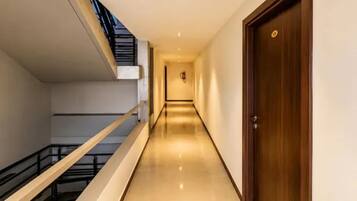 Un pasillo con una puerta de madera a la derecha, una escalera a la izquierda y un detector de incendios en la pared.