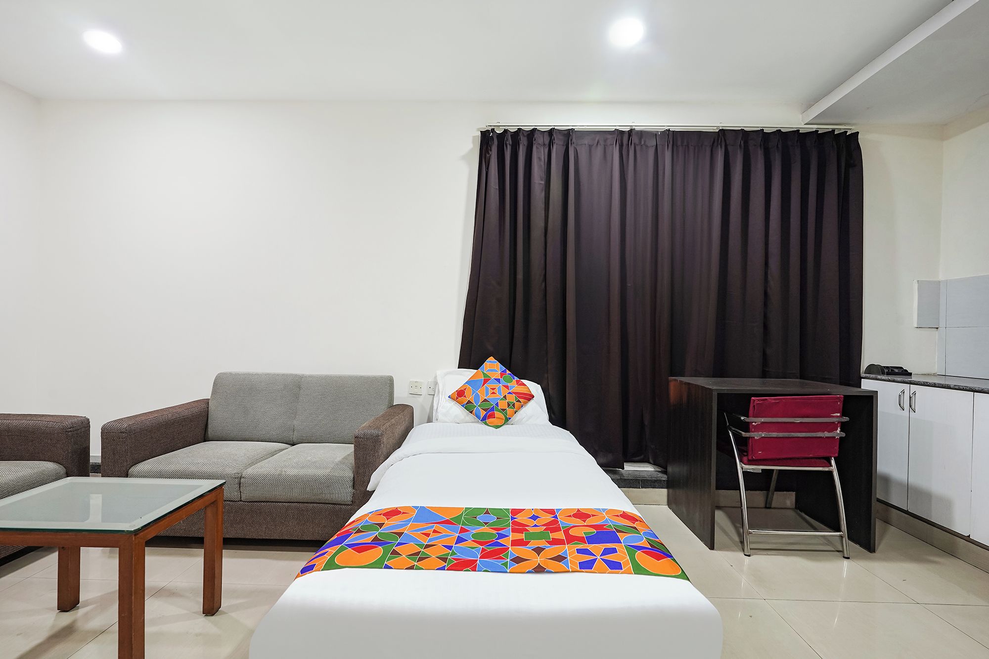 Una habitación de hotel con una cama, un sofá, una mesita y una zona de kitchenette.