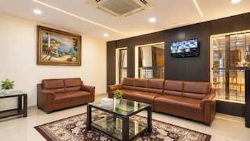 A modern living room with leather sofas, a glass coffee table, a painting, and a TV on the wall.