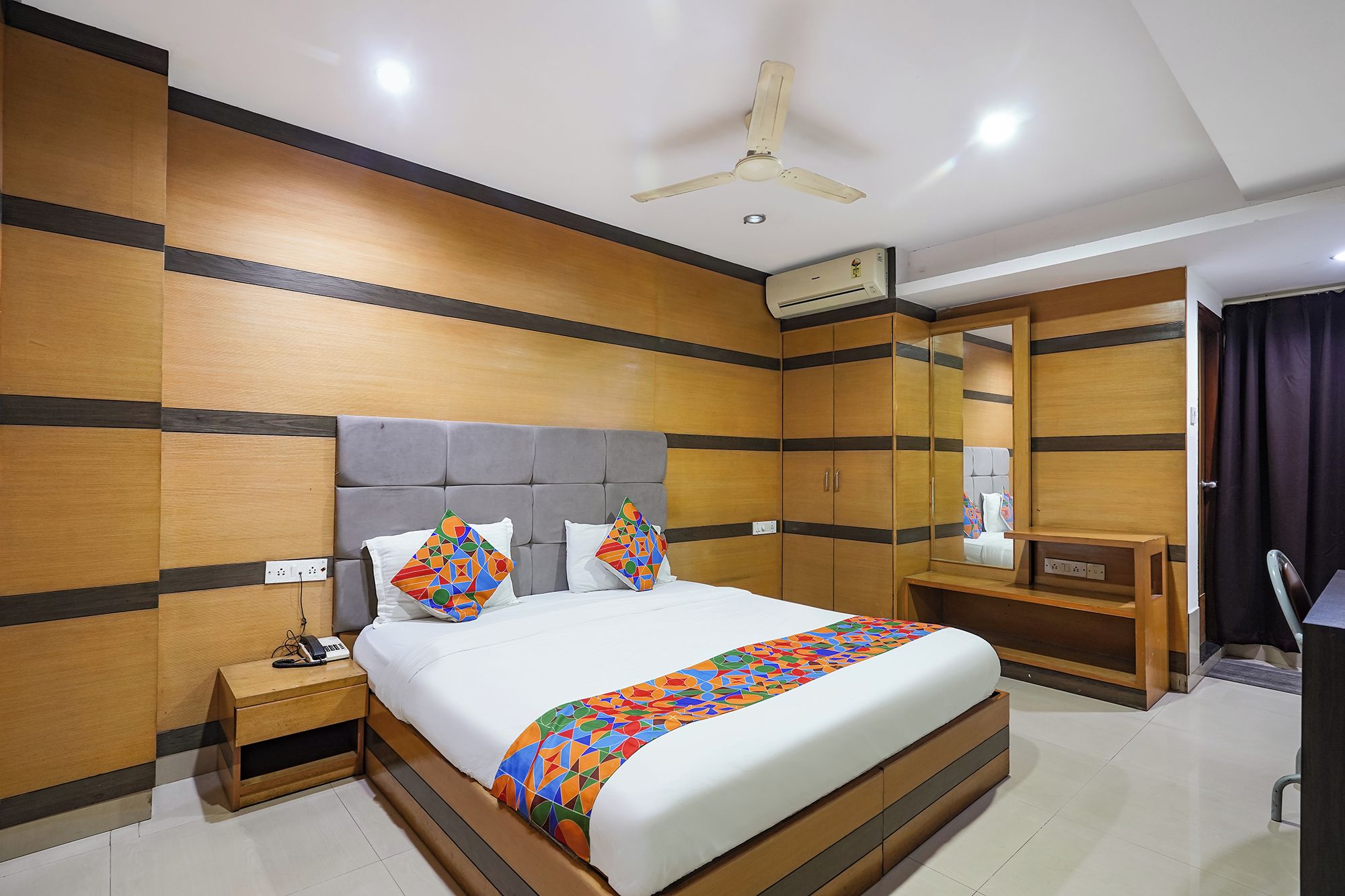 A hotel room with a bed, bedside table, nightstand, and a ceiling fan.