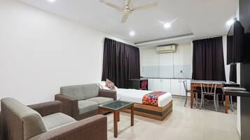 A hotel room with a bed, a sofa, a dining table, and a ceiling fan.